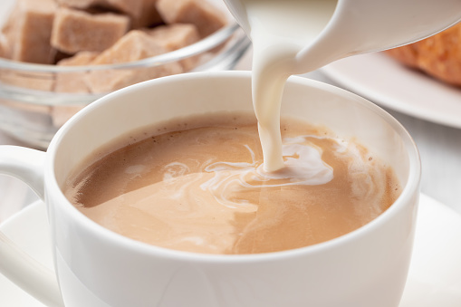 Pouring milk or cream into freshly brewed coffee, close up.