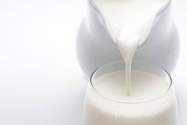 Pouring Milk Milk being poured from a white ceramic pitcher into a glass on a white background. cream dairy product stock pictures, royalty-free photos & images