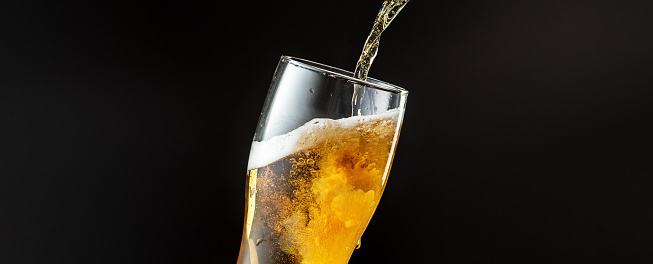 Pouring of cold and refreshing beer in glass with foam, horizontal flyer with copyspace for ad. Oktoberfest, drinks, alcohol, party concept. Brewed and crafted quality product on dark background.