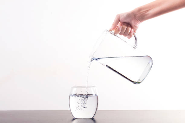 Pouring Water From Pitcher Into Glass, isolated on a white background with copy space stock photo