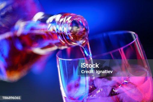 istock Pouring whiskey from bottle into glass with ice 1186896065