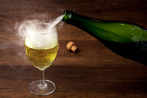 Pouring wine or champagne from the green bottle into the wine glass with some smoke on wooden background, for celebration or party stock photo