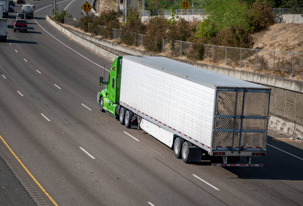Powerful big rig green bonnet semi truck transporting frozen cargo in refrigerated semi trailer driving on the wide multiline highway road stock photo