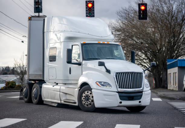 Powerful bonnet white big rig semi truck with dry van semi trailer turning on the city street crossroad with traffic light and crosswalk stock photo