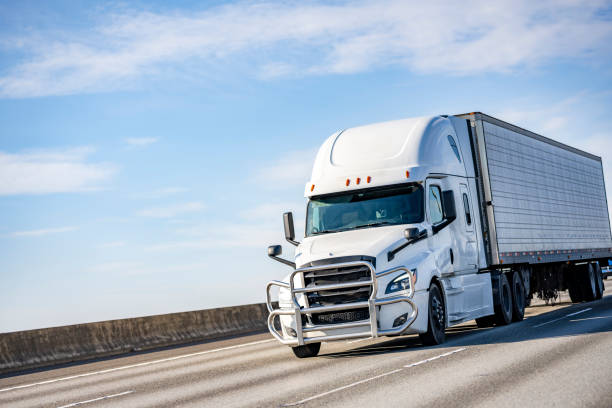 Powerful white big rig long haul industrial semi truck transporting goods in refrigerator semi trailer driving on the sunny multiline highway road stock photo