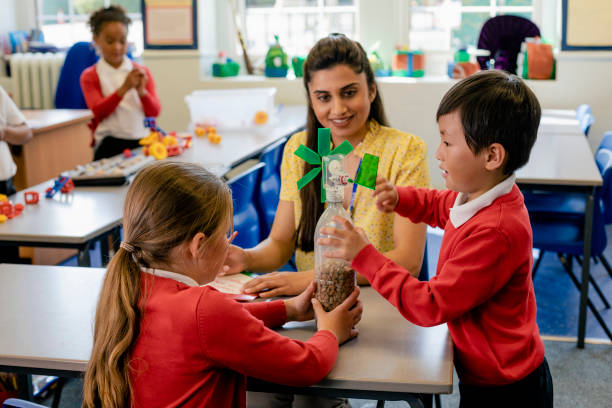 Practical Science Lesson A wide angle view of a teacher and her students during a hands-on practical science lesson she is teaching them and using interactive props to help them understand and learn. work as a teacher in the uk stock pictures, royalty-free photos & images