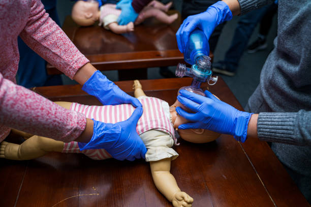 CPR practitioner examining airway passages on infant dummy. Model dummy lays on table and two doctors practice first aid. stock photo