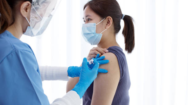Practitioner vaccinating woman patient in clinic. Doctor giving injection to adult woman at hospital. Nurse holding syringe and inject Covid-19 or coronavirus vaccine.Injection covid vaccine concept. stock photo