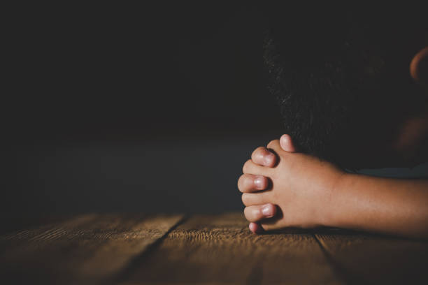 Praying hands of little boy on wooden table stock photo