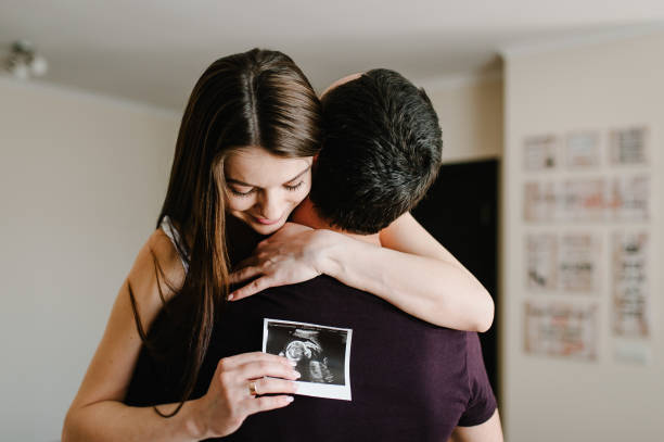 Pregnant couple holding in the hands ultrasound scan of their baby. A man, husband hugging his pregnant wife in the home. Happy family pregnancy, expectation. Black and white photo scan. stock photo