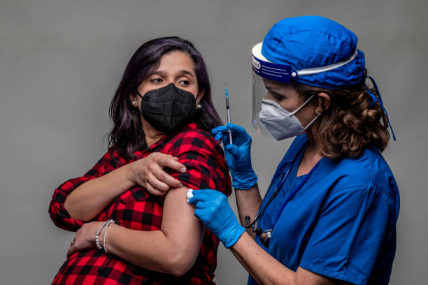 Pregnant hispanic mid adult woman receiving a covid 19 vaccine from a healthcare worker stock photo