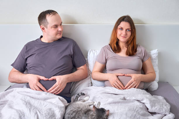 pregnant-wife-and-overweight-husband-lie-in-bed-holding-thei