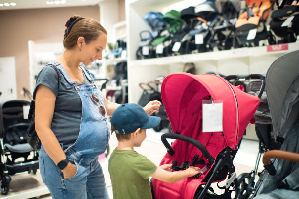 pregnant woman and her son choosing baby carriage in a store - babywinkel stockfoto's en -beelden