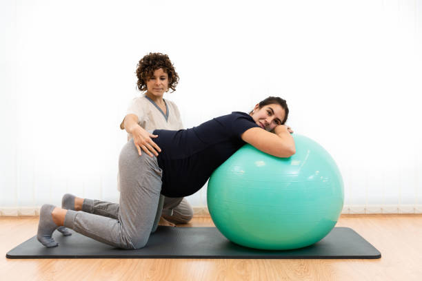 A pregnant woman doing pilates exercises with a ball with the help of her physiotherapist A pregnant caucasian woman doing pilates exercises with a ball with the help of her physiotherapist on the floor on a mat. Concept of physiotherapy pelvic floor treatment. pregnancy pelvic exercise stock pictures, royalty-free photos & images