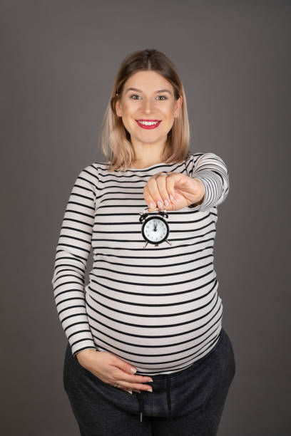 Pregnant woman holding a clock stock photo