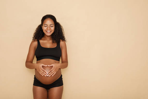 zwangere vrouw hand in hand op haar buik maken van een hartsymbool - pregnant stockfoto's en -beelden
