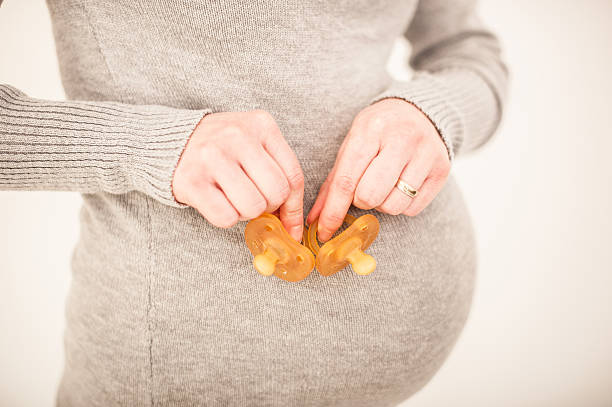 Pregnant Woman Holding two Pacifiers in her Hands stock photo
