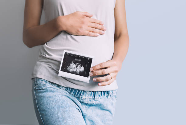 超音波赤ちゃんの画像を保持している妊婦。母親の手で妊娠中の腹とソノグラムの写真のクローズアップ。 - 診察　妊婦 ストックフォトと画像