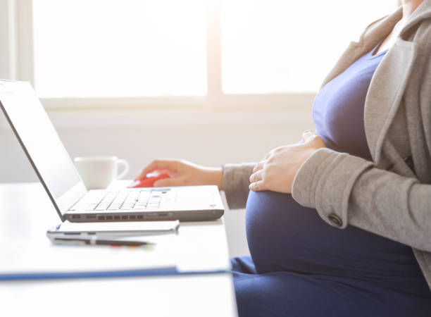 妊娠中の女性は、コンピュータのラップトップや携帯電話、ビジネスに取り組んでいます - 産休 ストックフォトと画像