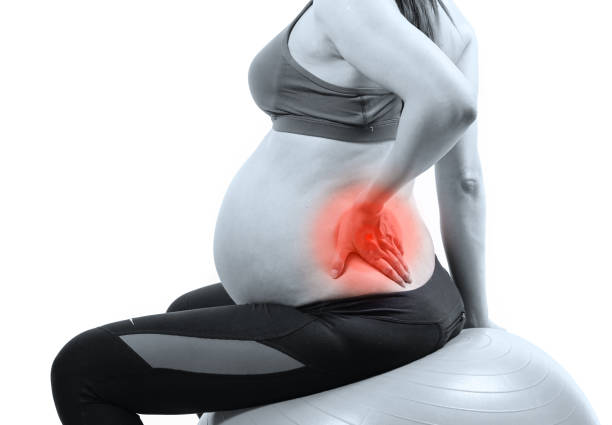 Pregnant woman on gymnastic ball holding her back in pain stock photo