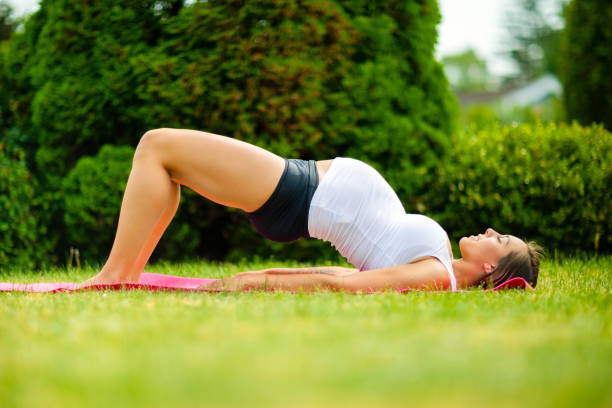 Pregnant Woman Practicing Bridge Pose On Grass stock photo