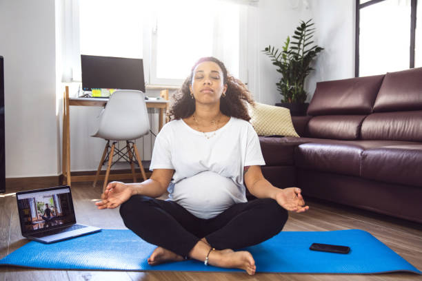 Pregnant woman practicing Yoga with online video class Pregnant woman practicing Yoga with online video class during Coronavirus pandemic lockdown. pregnancy exercises stock pictures, royalty-free photos & images