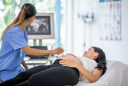 A pregnant woman smiles as the technician performs an ultrasound exam on her.