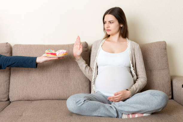 người phụ nữ mang thai ngồi trên ghế sofa từ chối ăn đồ ăn vặt như bánh rán và không cử chỉ. chế độ ăn uống lành mạnh cho khái niệm mẹ tương lai - mang thai hình ảnh sẵn có, bức ảnh & hình ảnh trả phí bản quyền một lần