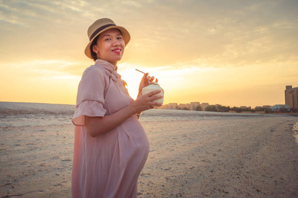 Pregnant woman spending time on the beach having fresh coconut by the seaside at sunset Cheerful pregnant Asian woman having fresh coconut and walking on the beach by the seaside and enjoying the sunset. Summer vacation during pregnancy hot arab woman stock pictures, royalty-free photos & images