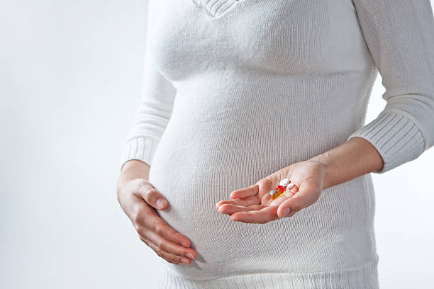 Pregnant woman touching belly and holding pills stock photo