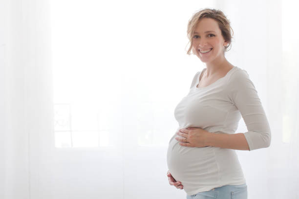 Pregnant woman touching belly looking at camera stock photo