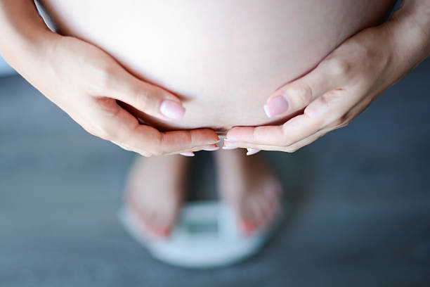 Pregnant woman weighing herself on a bathroom scale stock photo