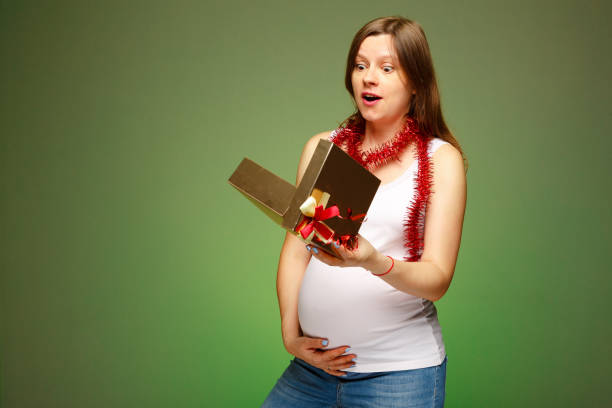 Pregnant woman with a gift, surprised face expression, getting present on Christmas eve. stock photo