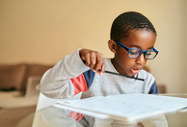 Preparing for a bright future ahead of him Shot of an adorable little boy doing his schoolwork at home boys glasses stock pictures, royalty-free photos & images