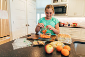A girl prepares a school lunch consisting of peanut butter and jelly sandwich, chips, cookies, fruit, carrots and putting them in plastic bags.