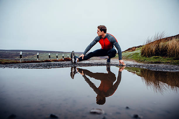 Preparing to run! Male runner training outdoors in wet weather. His reflection seen in a puddle of water before him. He stretched his leg. moor photos stock pictures, royalty-free photos & images