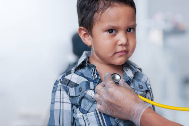 A preschool age boy getting a heart screening, using a stethoscope on chest with a buttoned down shirt. stock photo