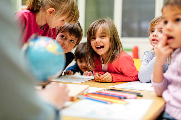 Preschool teacher and children using globe. Preschool teacher teaching her children about geography. Using globe and asking the questions. Children sitting by the table and listen teacher carefully. Models in this shot are part of real kindergarten group and their teacher. preschool stock pictures, royalty-free photos & images