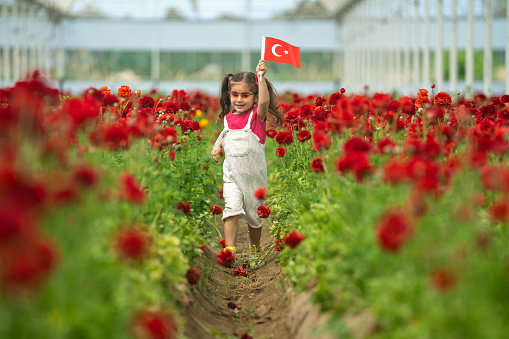 Photo of preschooler girl holding Turkish flag in flower garden celebrating April 23 National Sovereignty and Children's Day, that is Ulusal Egemenlik ve Çocuk Bayramı. Shot under daylight.