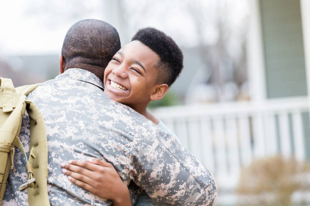 Preteen boy reunites with military dad African American preteen boy hugs his dad in the front yard. His dad has return from overseas military assignment. soldiers returning home stock pictures, royalty-free photos & images