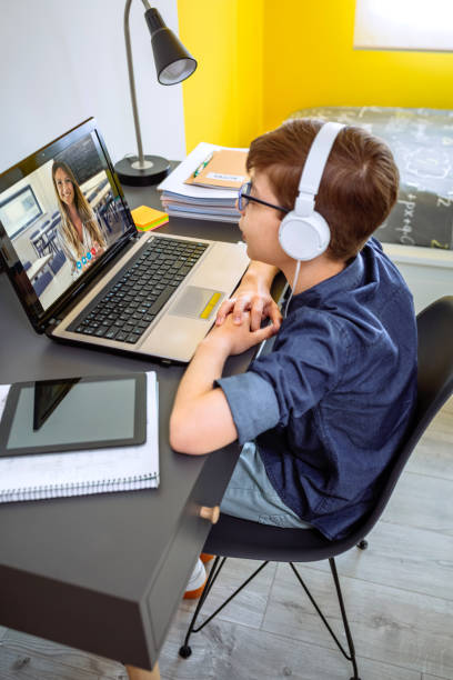 Preteen with headphones receiving class at home with laptop from his bedroom stock photo