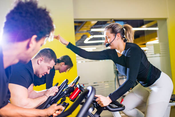 Pretty authentic female instructor with headset in fitness class exercise with group in cycling room stock photo