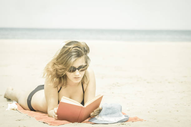 pretty girl in bikini reading book on beach and sunbathing stock photo