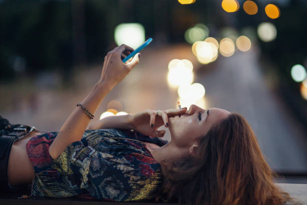 Pretty girl smoking Girl browsing on her mobile phone, smoking a cigarette and lying on a parapet little girl smoking cigarette stock pictures, royalty-free photos & images