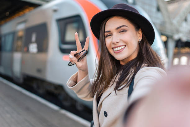Pretty girl tourist takes selfie at the railway station against the background of the locomotive. Girl talking on video call Pretty girl tourist takes selfie at the railway station against the background of the locomotive. Girl talking on video call railroad station photos stock pictures, royalty-free photos & images