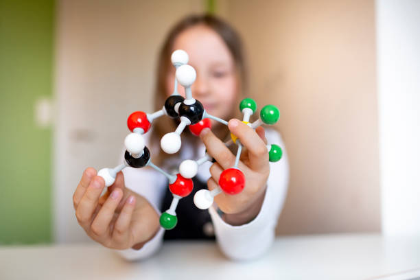 pretty schoolgirl with black dungarees sits in her room and learns on a model for molecules stock photo