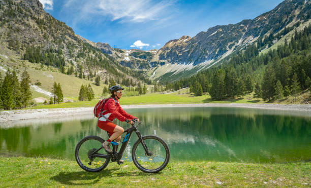 pretty senior woman on electric mountain bike pretty senior woman riding her electric mountain bike at the Seealp lake in the Nebelhorn area above  Oberstdorf, Allgau Alps, Bavaria, Germany  Electric bike stock pictures, royalty-free photos & images