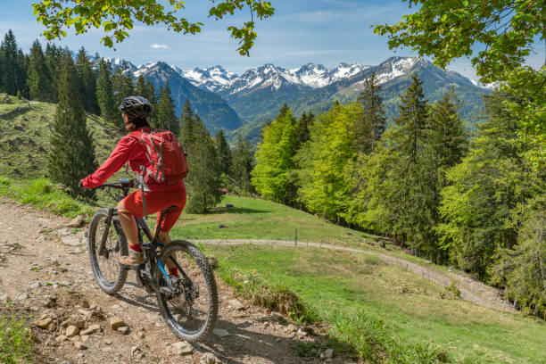 pretty senior woman on electric mountain bike pretty senior woman riding her electric mountain on warm spring day with snoe capped mountains on the Wallraff Trail in the Nebelhorn area above  Oberstdorf, Allgau Alps, Bavaria, allgau alps stock pictures, royalty-free photos & images