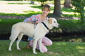 Pretty smiling blonde kneeling with her labrador in the park on a sunny day
