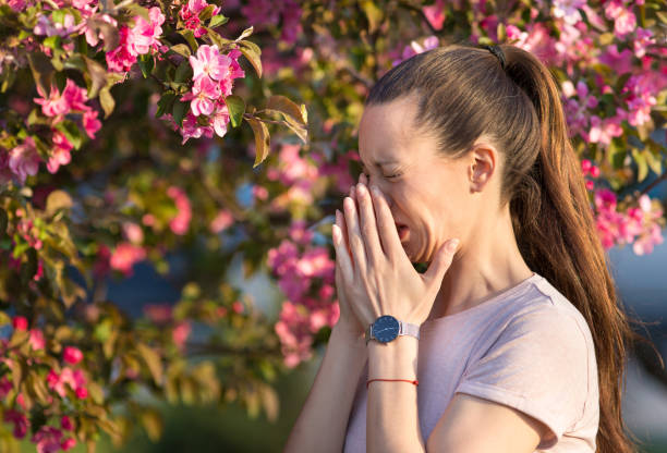 Pretty woman sneezing in front of blooming tree Young pretty woman sneezing in front of blooming tree. Spring allergy concept antihistamine stock pictures, royalty-free photos & images